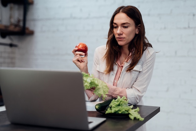 栄養学の医師はオンラインで相談します。女性栄養士がノートパソコンの前の机に座って、ライブビデオ通話で話します。