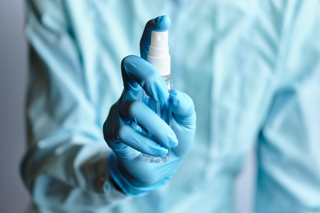 A doctor in a dressing gown and medical gloves shows how to use an antiseptic sanitizer.