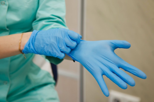 Doctor in dressing gown puts on sterile blue gloves. Concept of hero of doctors and stress. Concept of infection control. Risk of infection spreading. Copy space