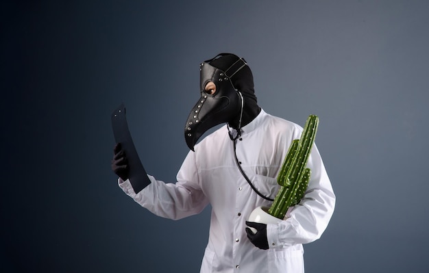 A doctor in a dressing gown, wearing a plague doctor mask with a cactus in his hands