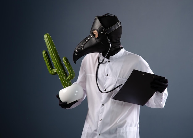 A doctor in a dressing gown, wearing a plague doctor mask with a cactus in his hands