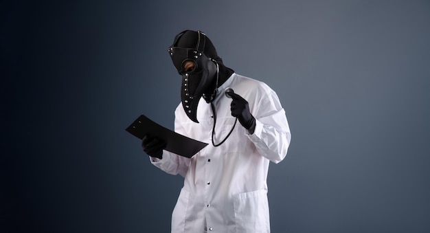 A doctor in a dressing gown wearing a plague doctor mask with a stethoscope in his hands