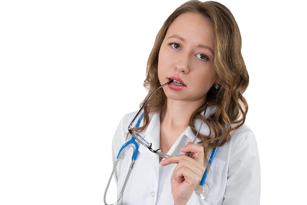 A doctor in a dressing gown and with a stethoscope around his neck nibbles on the shackle of his glasses Isolated on white background