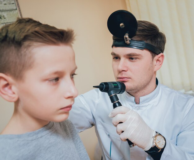 Doctor examines boy ear with otoscope.