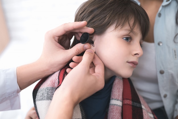 Doctor examines the ear of a sick boy.