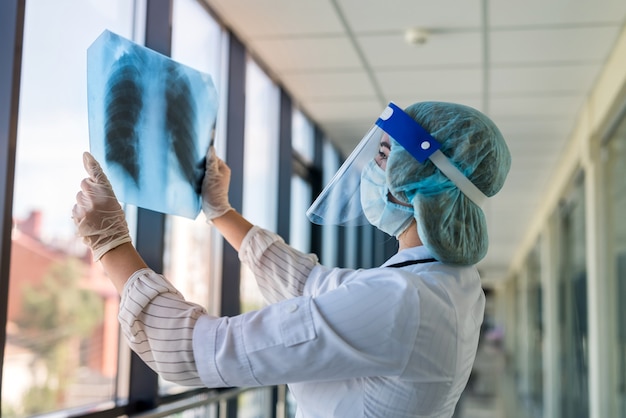 Doctor examines x-ray image of lungs in face shield and mask to determine pneumonia caused by a new virus covid19