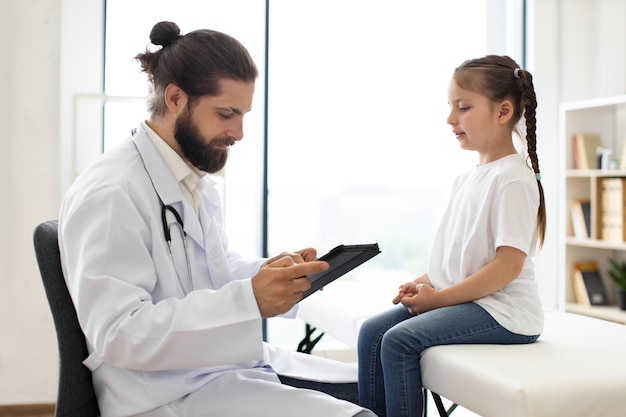doctor examines young girl and records medical data on tablet