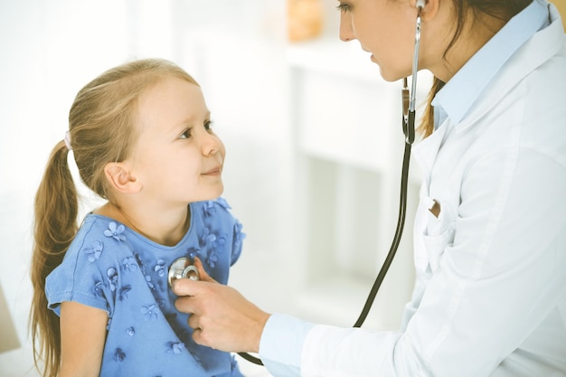 doctor examining a child by stethoscope. happy smiling girl patient dressed in blue dress is at usual medical inspection. medicine concept.