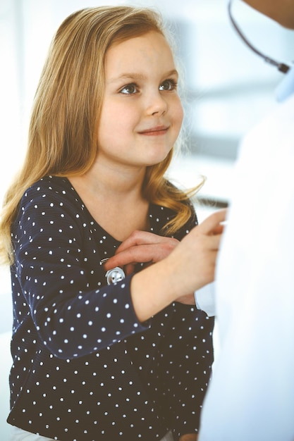 Doctor examining a child patient by stethoscope. Cute baby girl at physician appointment. Medicine concept. Toned photo