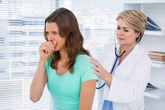 Doctor examining coughing patient with stethoscope