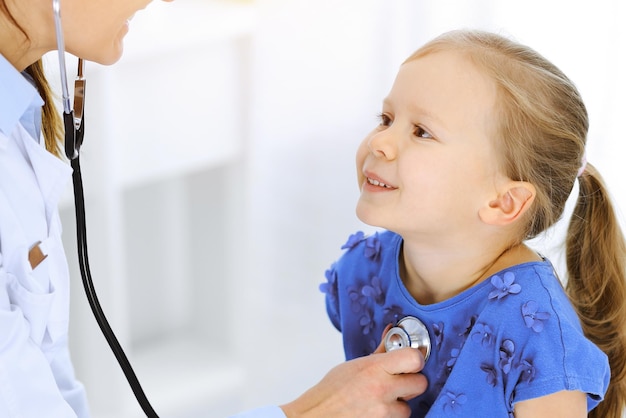 Doctor examining a little girl by stethoscope. Happy smiling child patient at usual medical inspection. Medicine and healthcare concepts.