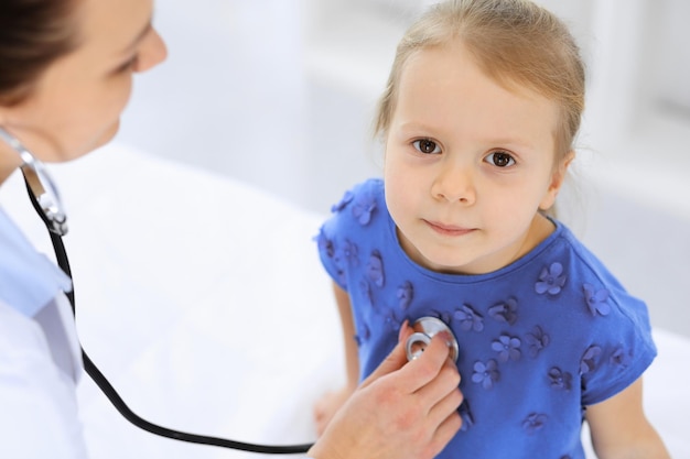 Doctor examining a little girl by stethoscope. Happy smiling child patient at usual medical inspection. Medicine and healthcare concepts.