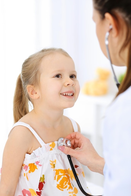 Doctor examining a little girl by stethoscope. Happy smiling child patient at usual medical inspection. Medicine and healthcare concepts.