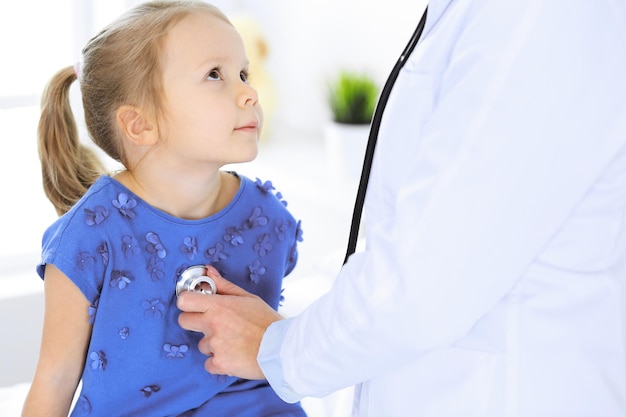 Doctor examining a little girl by stethoscope. Happy smiling child patient at usual medical inspection. Medicine and healthcare concepts.