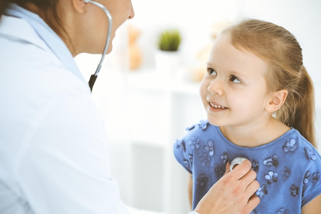 Doctor examining a little girl by stethoscope Happy smiling child patient at usual medical inspection Medicine and healthcare concepts