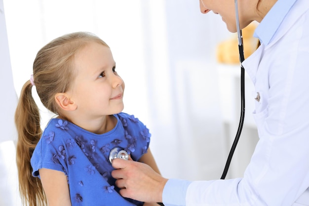 Доктор осматривает маленькую девочку с помощью стетоскопа. Счастливый улыбающийся ребенок-пациент на обычном медицинском осмотре. Концепции медицины и здравоохранения.