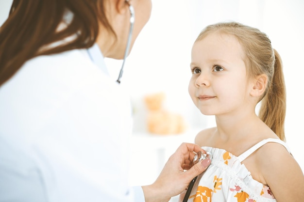 Doctor examining a little girl by stethoscope. Happy smiling child patient at usual medical inspection. Medicine and healthcare concepts.