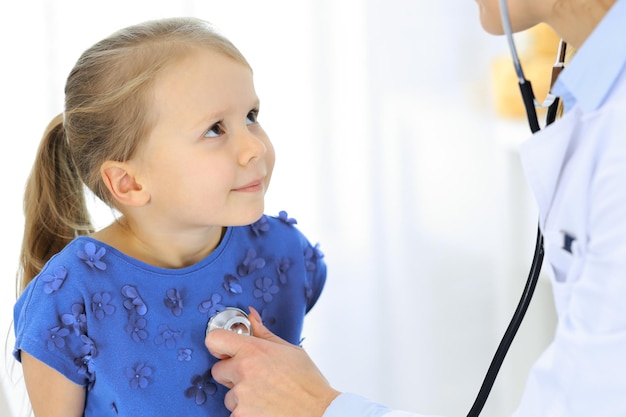 Photo doctor examining a little girl by stethoscope happy smiling child patient at usual medical inspection medicine and healthcare concepts