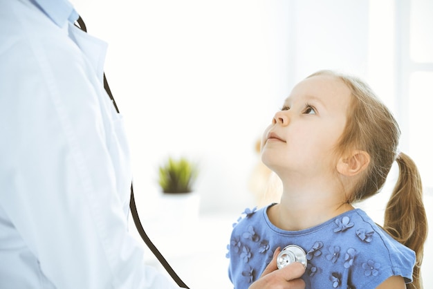 Doctor examining a little girl by stethoscope Happy smiling child patient at usual medical inspection Medicine and healthcare concepts