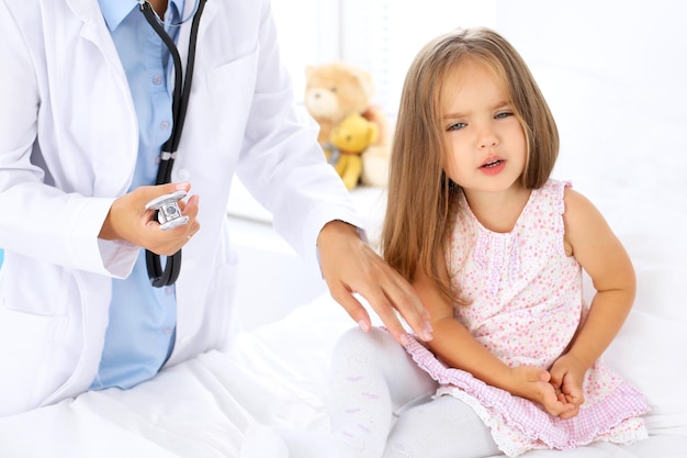 Photo doctor examining a little girl by stethoscope. patient turned away from his physician.