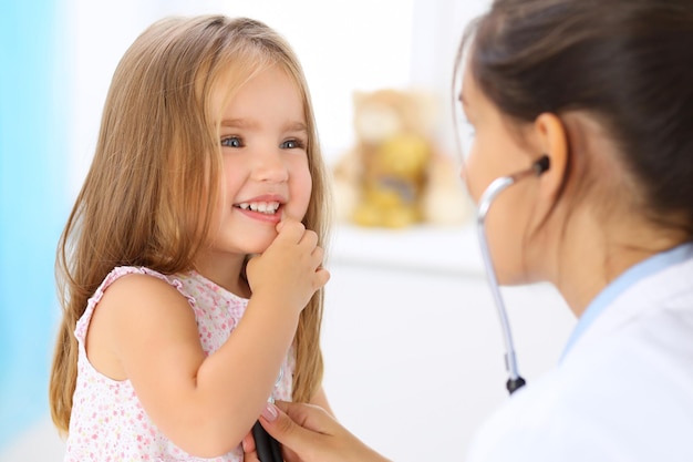 Доктор осматривает маленькую девочку с помощью стетоскопа.