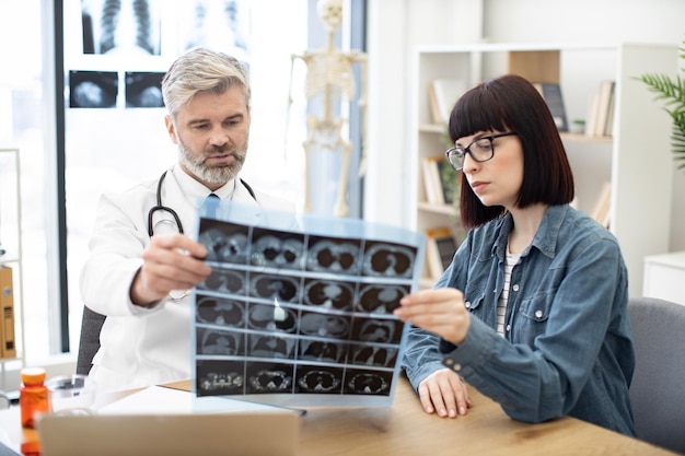 Doctor examining MRI scans while woman sitting at desk