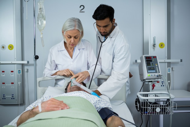 Medico ed esaminando un paziente con lo stetoscopio e posizionando una maschera di ossigeno