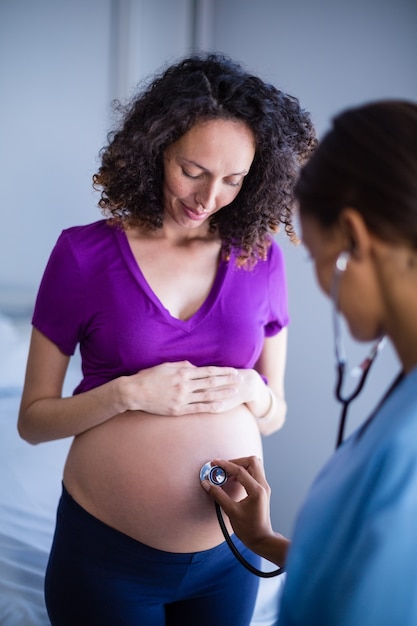 Доктор изучения живот беременной женщины с стетоскоп в палате
