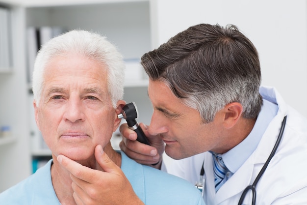 Doctor examining senior patients ear with otoscope