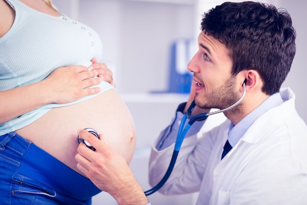 Doctor examining stomach of standing pregnant patient