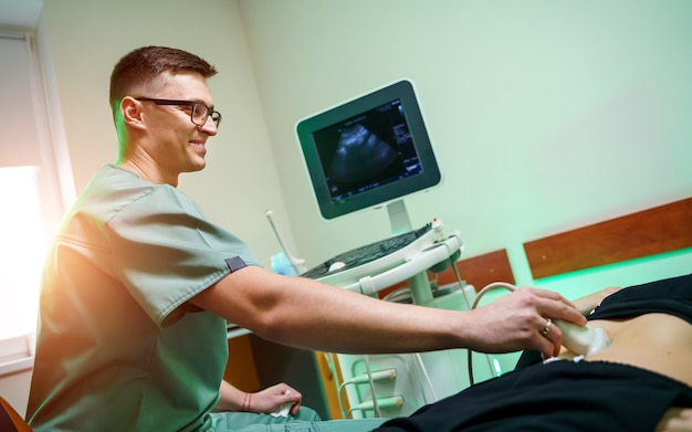 Photo doctor examining a woman with ultrasonic equipment at hospital. closeup of a cheerfull male medician with special equipment.