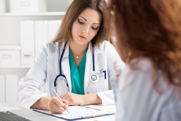 Doctor filling medical form while patient consultation. Patient sitting at doctor office. Diagnostic and prevention of women diseases, healthcare and medical service concept