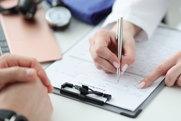 Doctor filling out patients medical history in clinic closeup