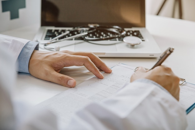 Doctor filling up medical form while sitting at the desk in hospital office. Physician at work. 