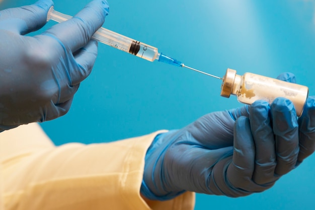 Doctor fills a syringe with medicine on blurred blue background