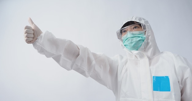 Доктор жест Азиатская женщина-врач в костюме СИЗ или средства индивидуальной защиты жестикулирует и указывает. белые медицинские резиновые перчатки. защитные очки и зеленая маска N95 для защиты от пандемии коронавируса.