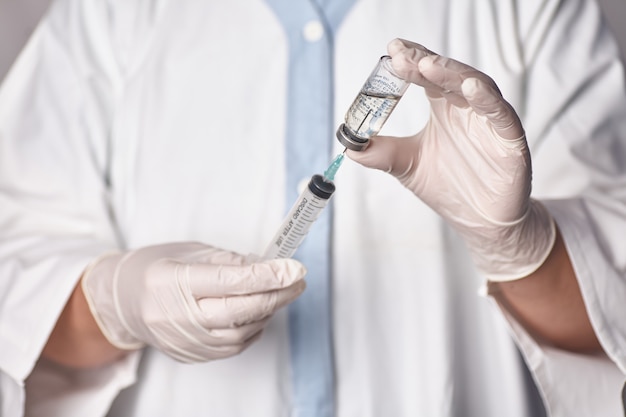 The doctor gets the vaccine into the syringe. Glass bottle in a technician's hand. A bottle with a cure holds a hand in silicone gloves. A breakthrough in treatment. Vaccine medical exams. Pandemic.