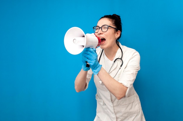 Doctor girl in uniform shouting into loudspeaker on blue background