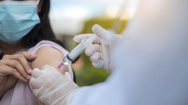 Doctor giving antiviral injection to patient. Woman in medical face mask getting Covid-19 or flu vaccine at field hospital.