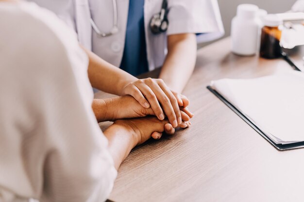 Doctor giving hope Close up shot of young female physician leaning forward to smiling elderly lady patient holding her hand in palms Woman caretaker in white coat supporting encouraging old person