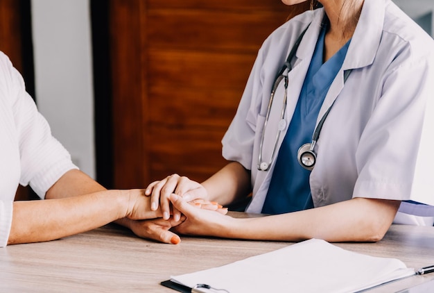 Doctor giving hope Close up shot of young female physician leaning forward to smiling elderly lady patient holding her hand in palms Woman caretaker in white coat supporting encouraging old person