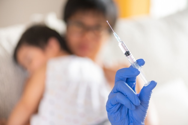 Doctor giving an injection vaccine to a girl with her mother on background.