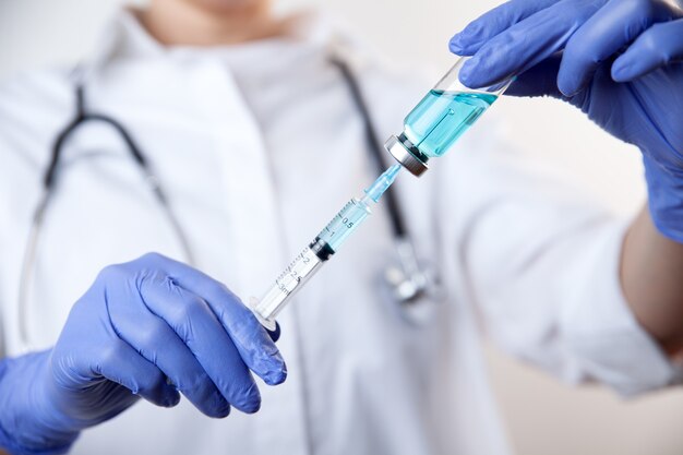 Photo doctor in gloves filling up syringe from bottle with vaccine medicine