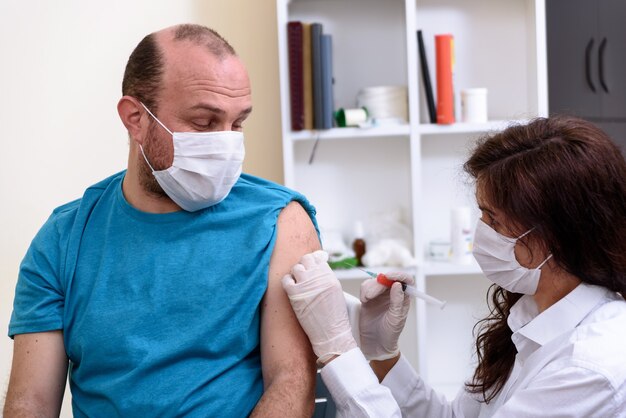 Doctor in gloves holding syringe and making injection to patient in medical mask.