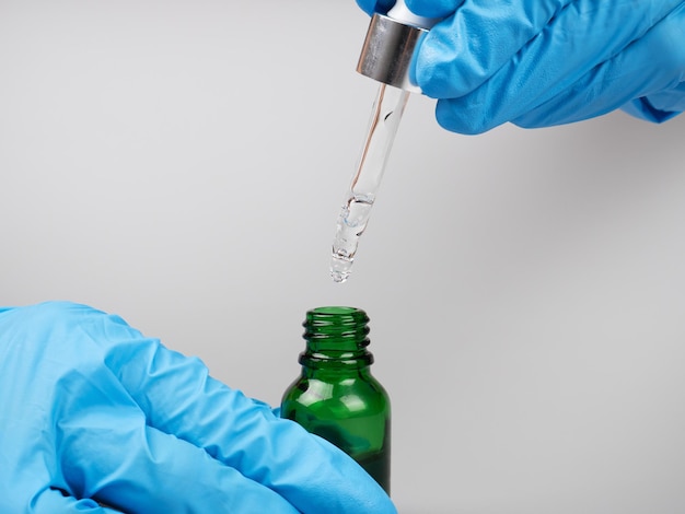 A doctor in gloves holds a pipette and a bottle of medicine in his hands