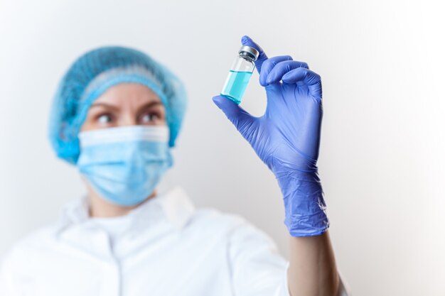 Doctor in gloves and mask holds bottle with vaccine, medicine