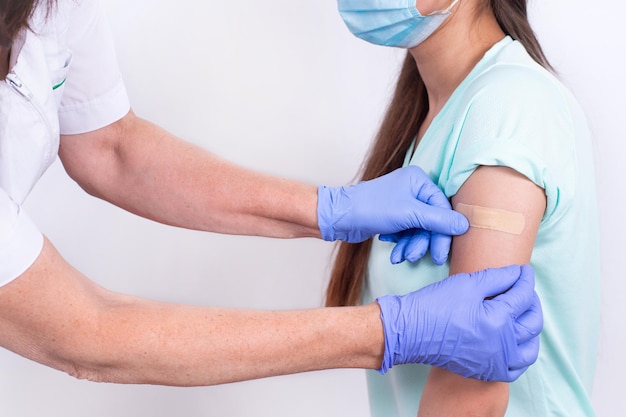 Doctor glues bandage on patients shoulder after an injection or vaccination closeup vaccination