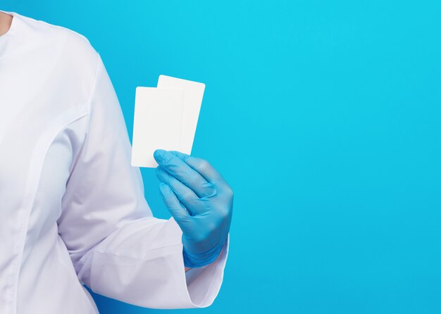 Doctor hand in blue medical latex gloves holds an empty paper business card on a blue surface