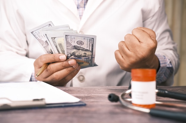 Doctor hand counting cash with pill container on table