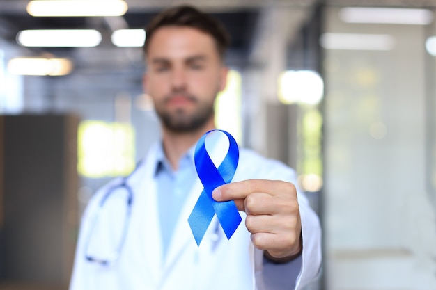 Doctor hand with blue prostate cancer awareness ribbon. Medicine oncology closeup sky symbol.